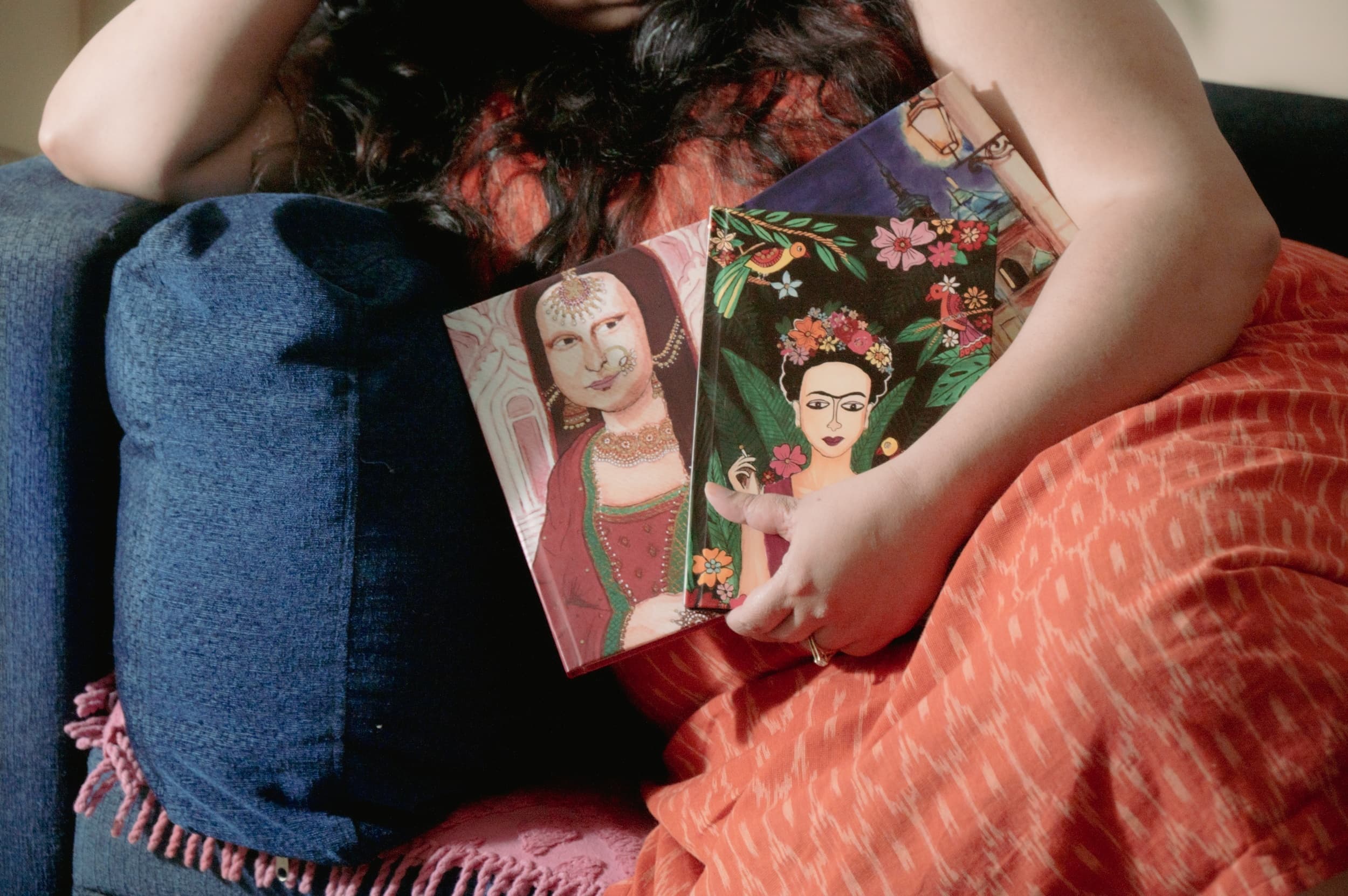 A close-up of illustrated notebook covers held in the crook of an arm