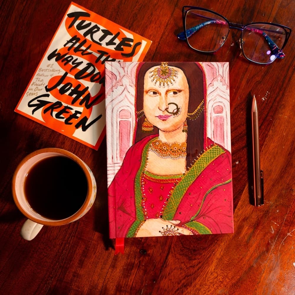An illustrated journal styled with a paperback book, coffee cup, and pen on a wood table