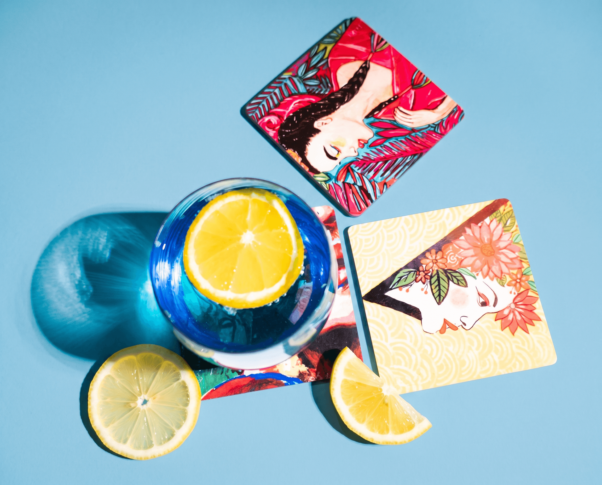 Two illustrated coasters styled with a citrus drink and lemon wedges against a powder-blue background
