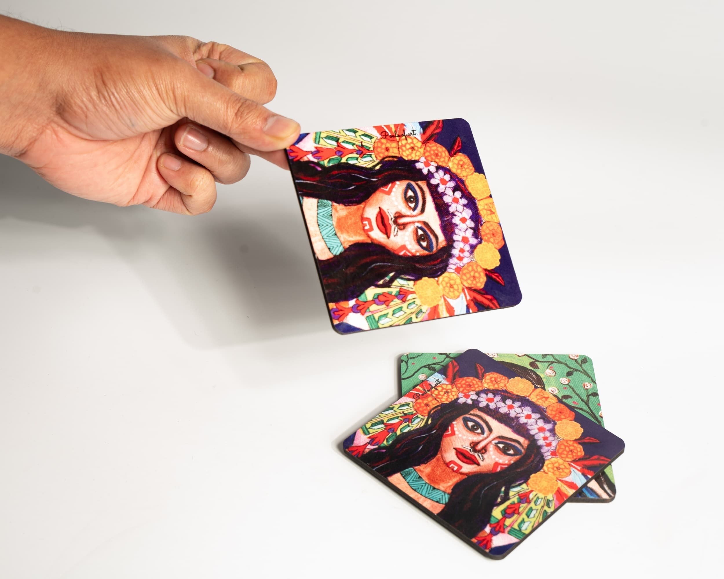 A hand holding an illustrated coaster above a stack of coasters