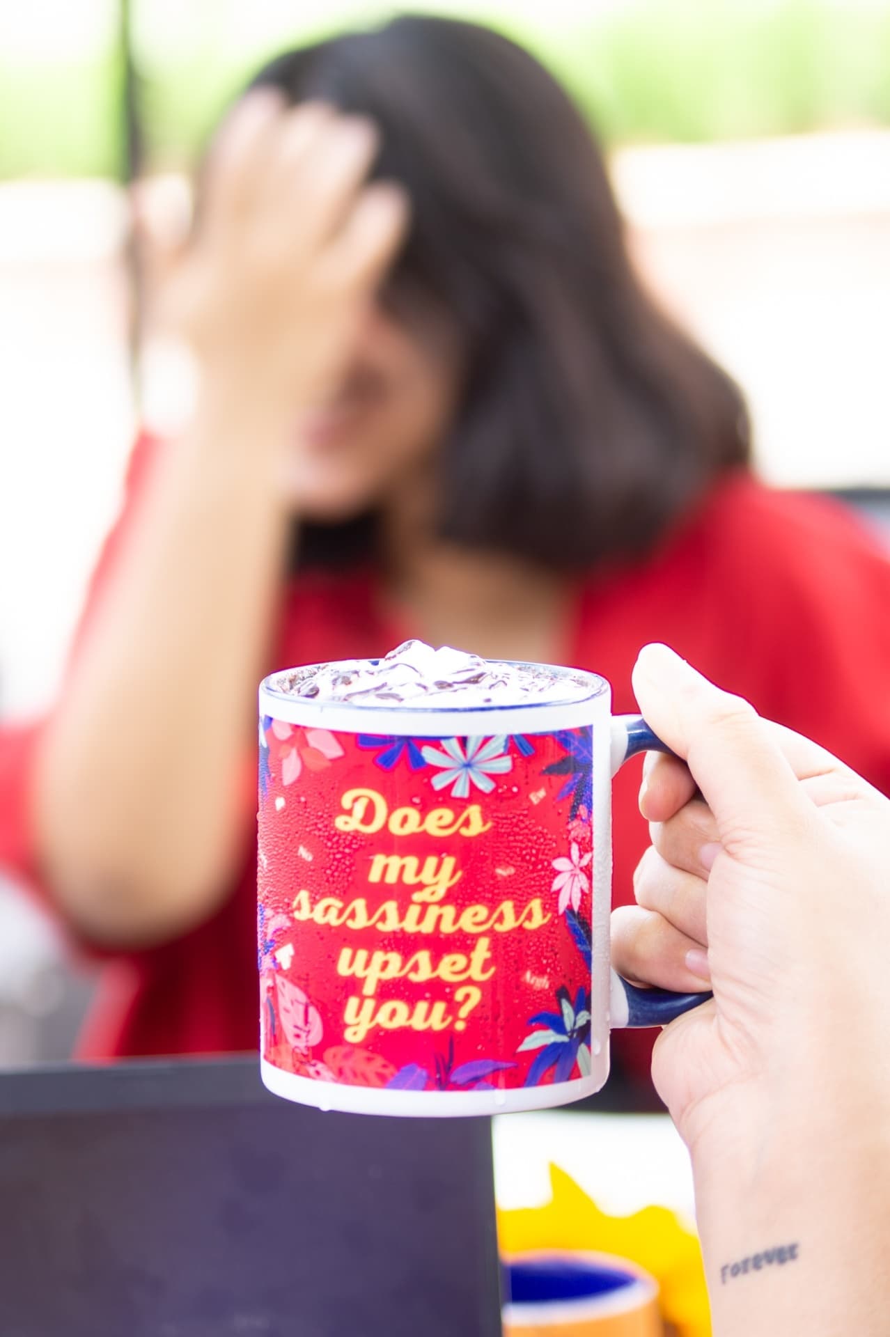A woman covering her face while holding up a mug printed with 'Does my sassiness upset you?' and a floral design
