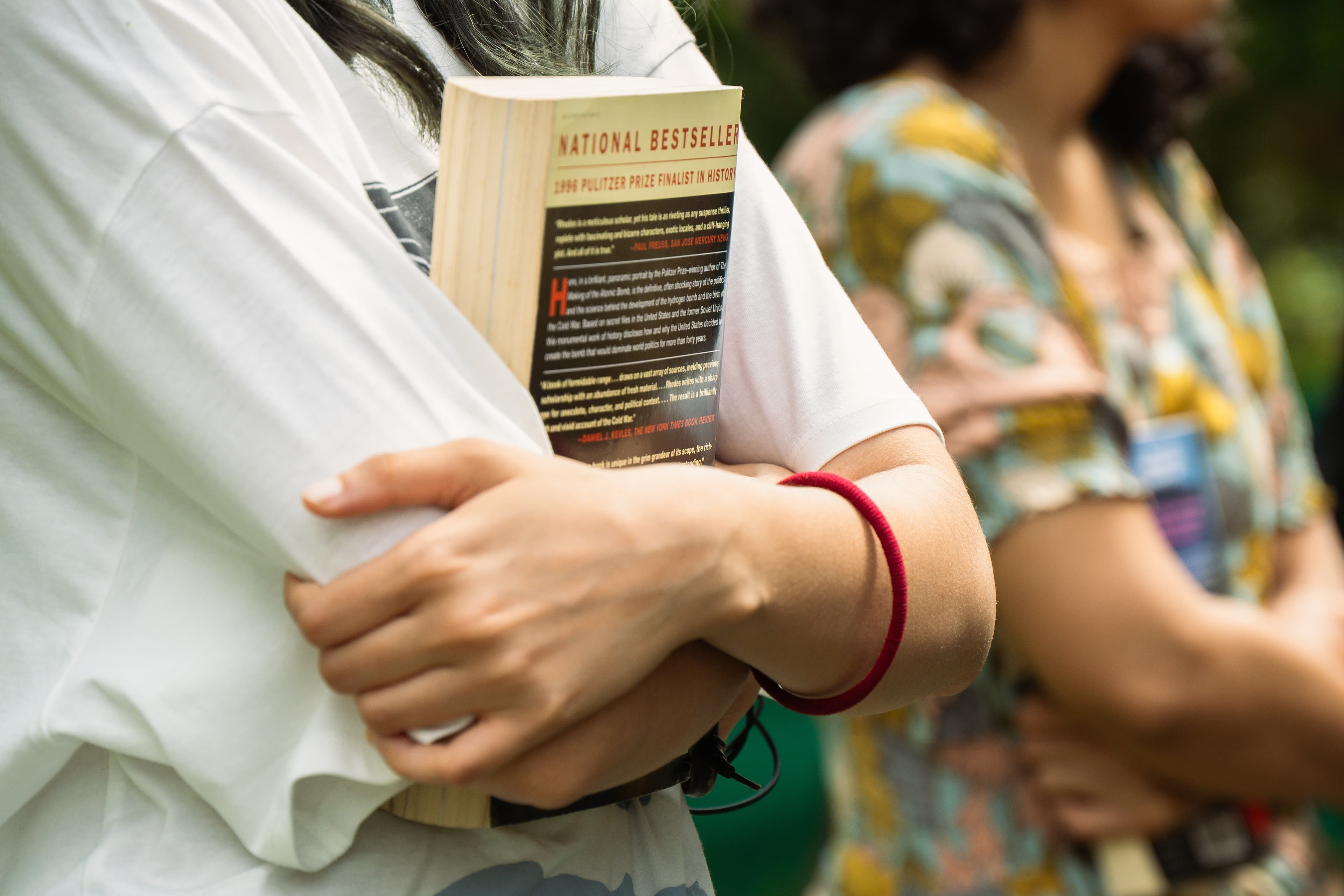 A man carrying a nonfiction paperback tucked under his arm while walking outdoors