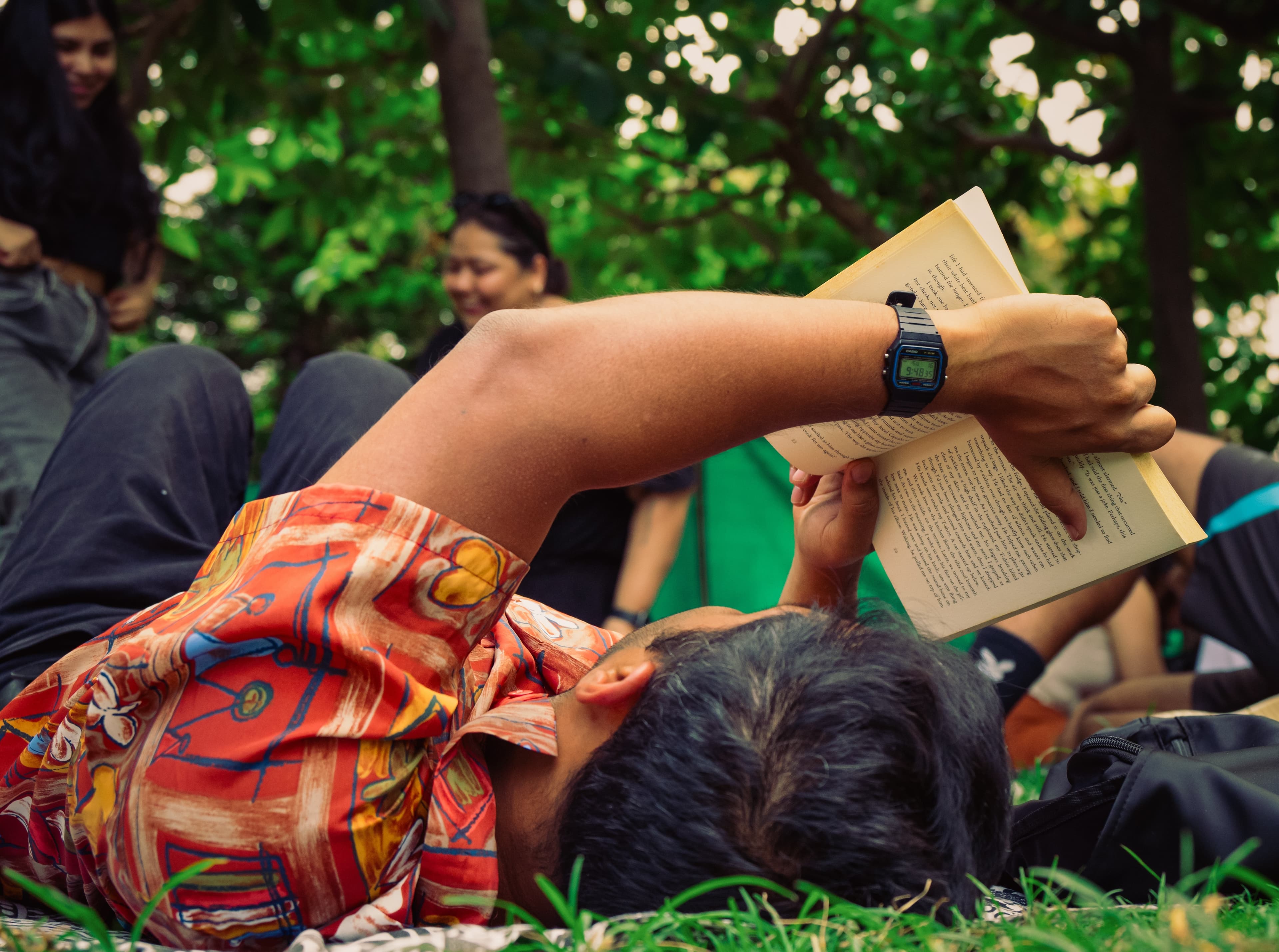 A man lying on grass reading a paperback held above his face