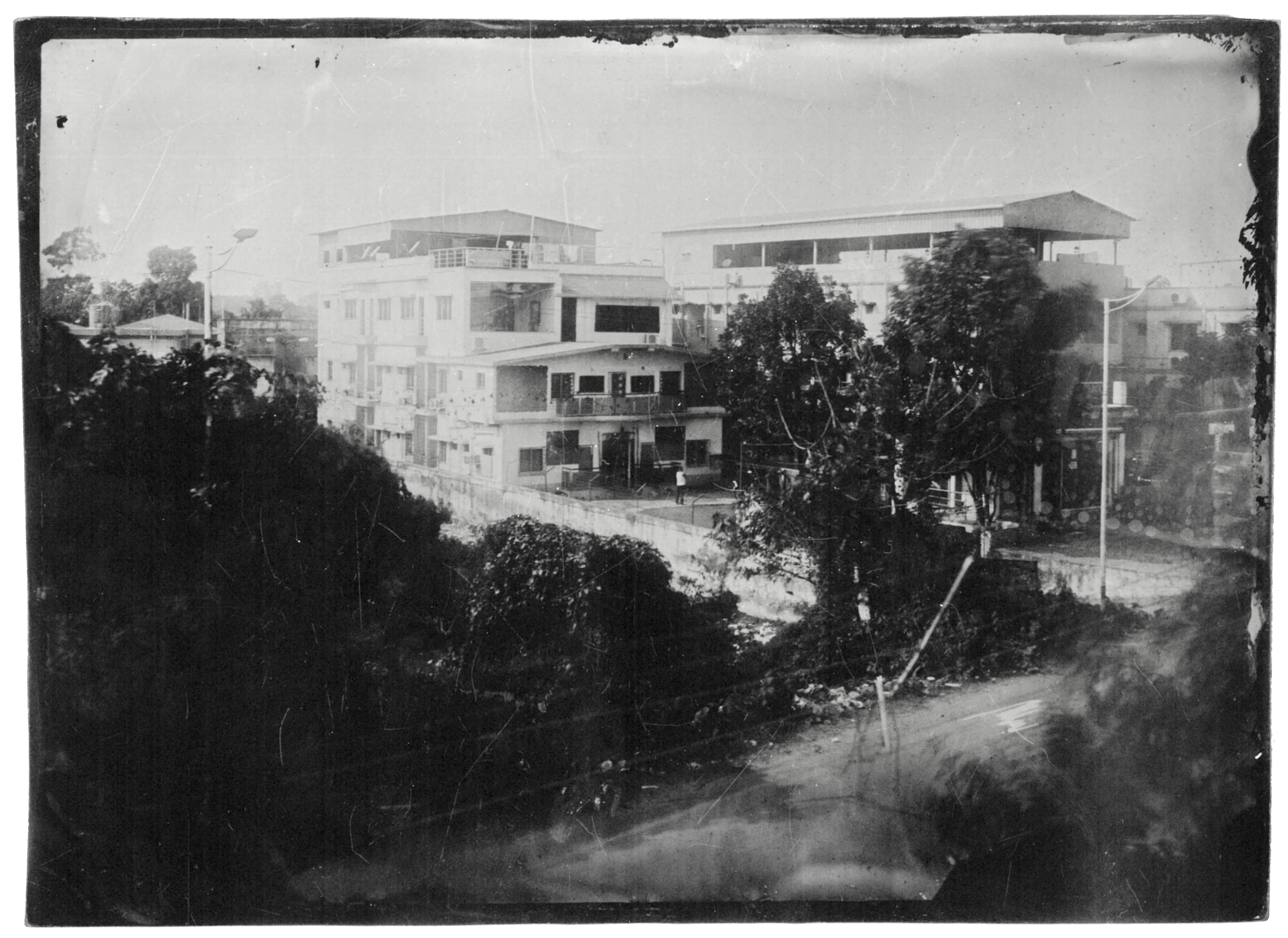 A wet plate collodion image of a residential building seen from a hillside, framed by trees and a sloping road