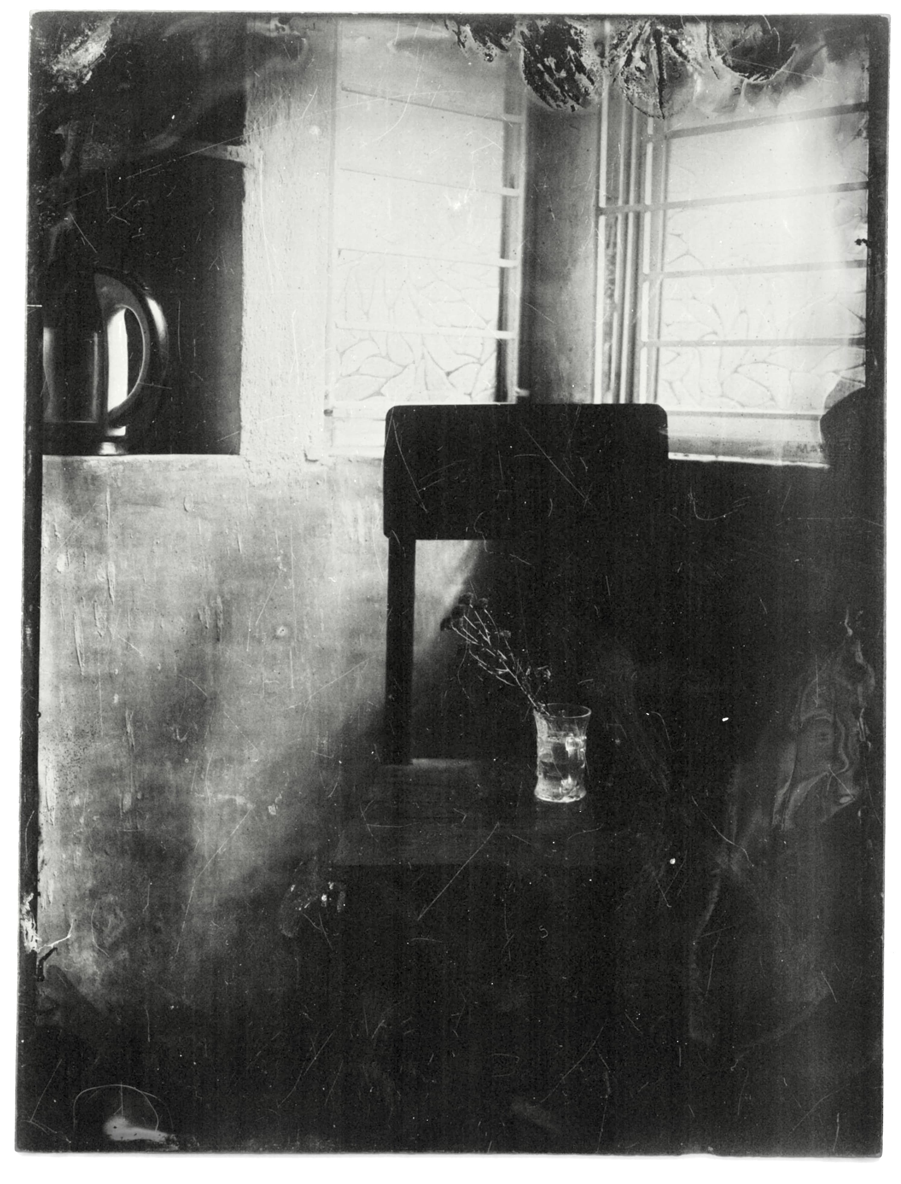 A wet plate collodion still life of a wooden stool by a window, a sprig of flowers in a glass on the seat