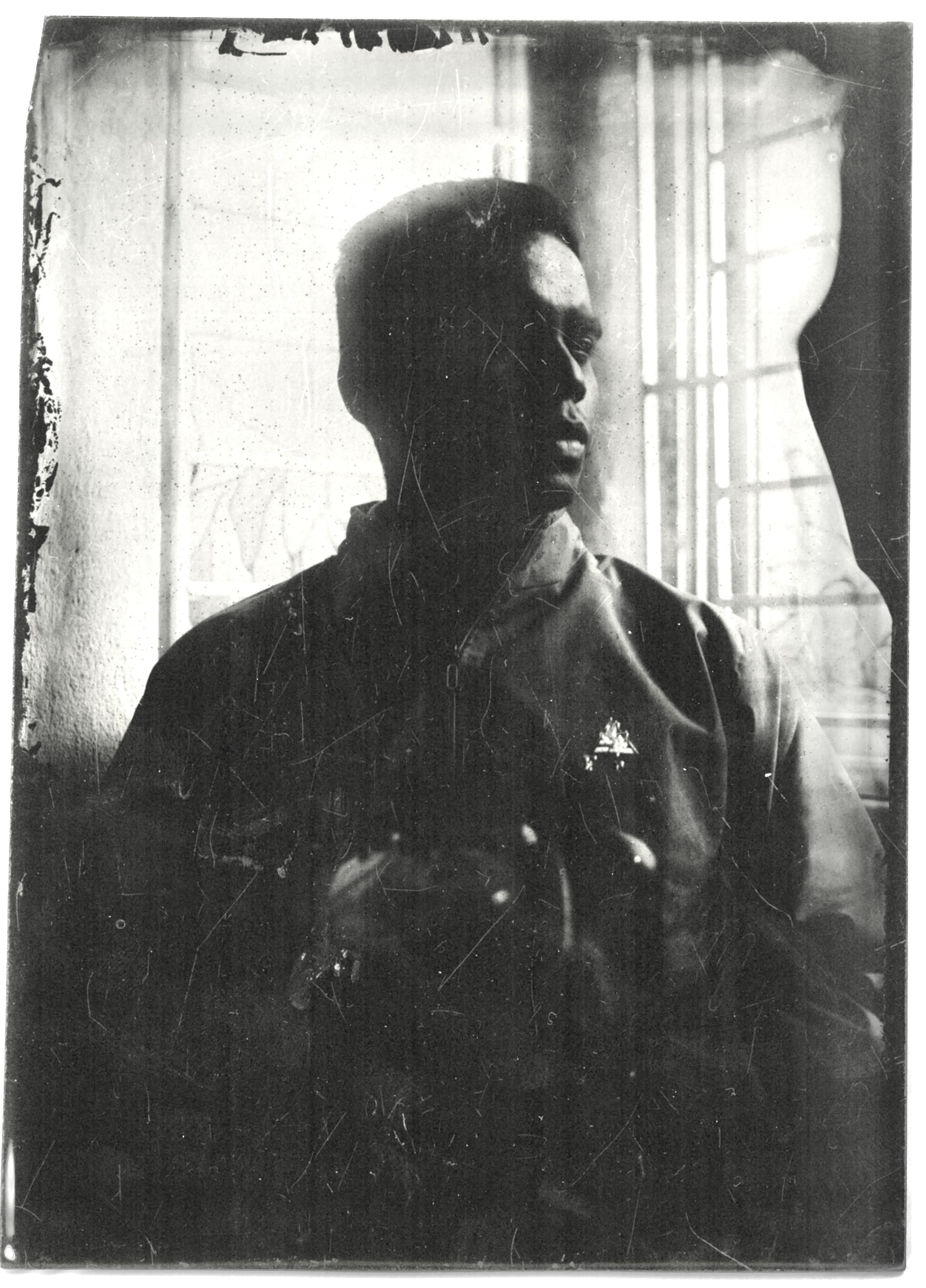 A wet plate collodion portrait of a man in silhouette against a bright window, edges of the plate stained and scratched