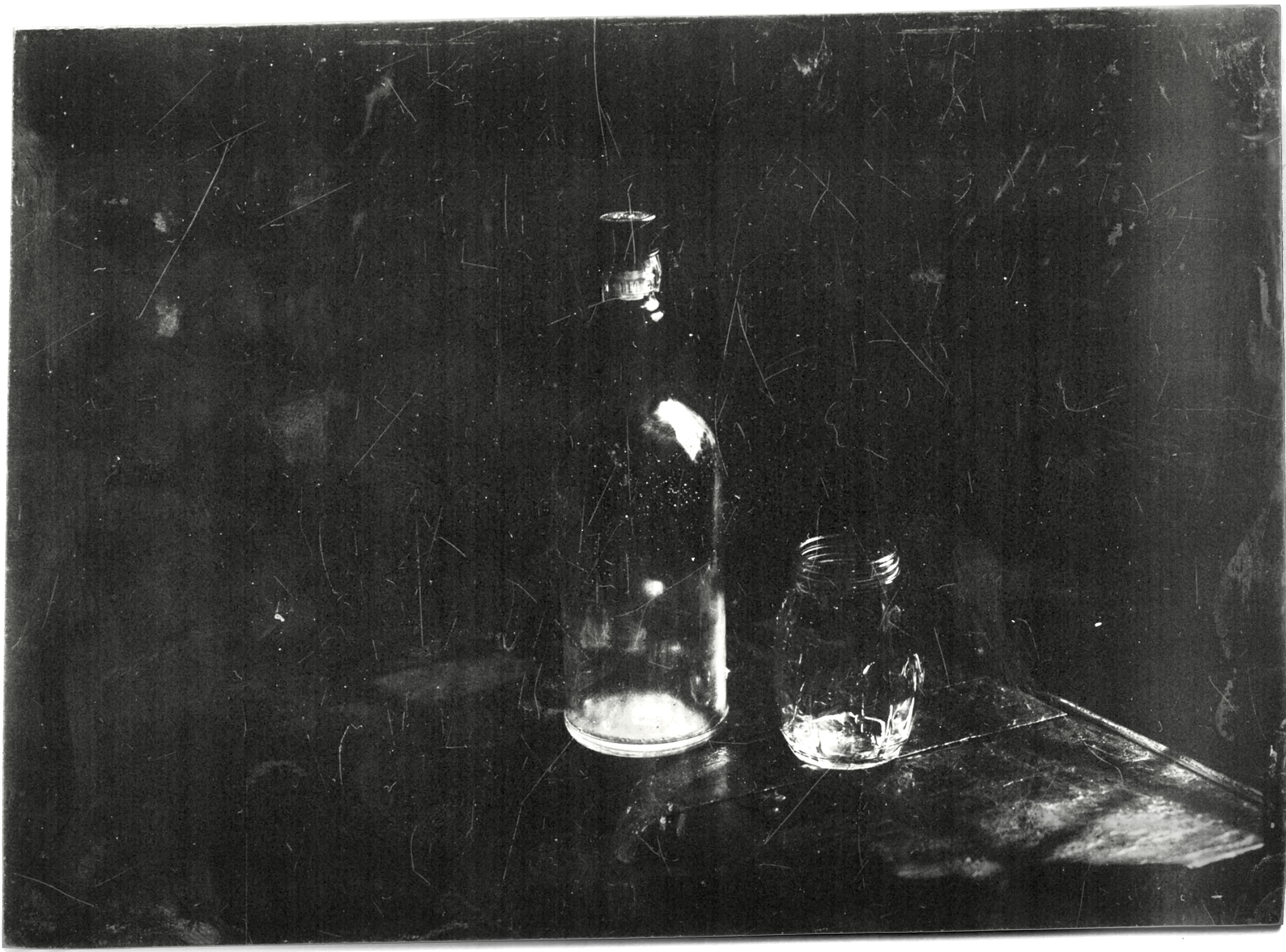 A wet plate collodion still life of a glass bottle and jar on a dark wooden table