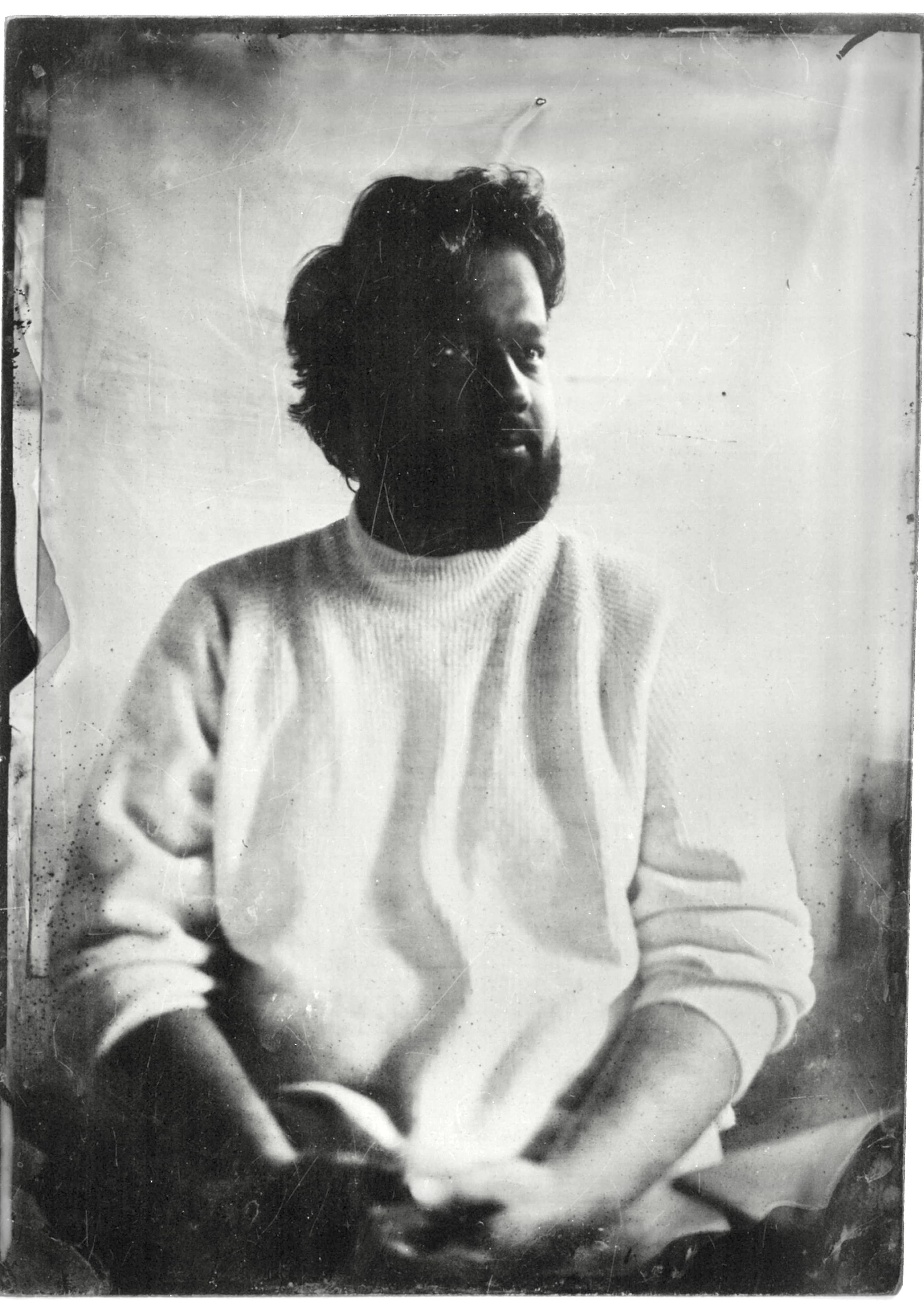 A wet plate collodion portrait of a bearded man in a white sweater, seated against a plain backdrop