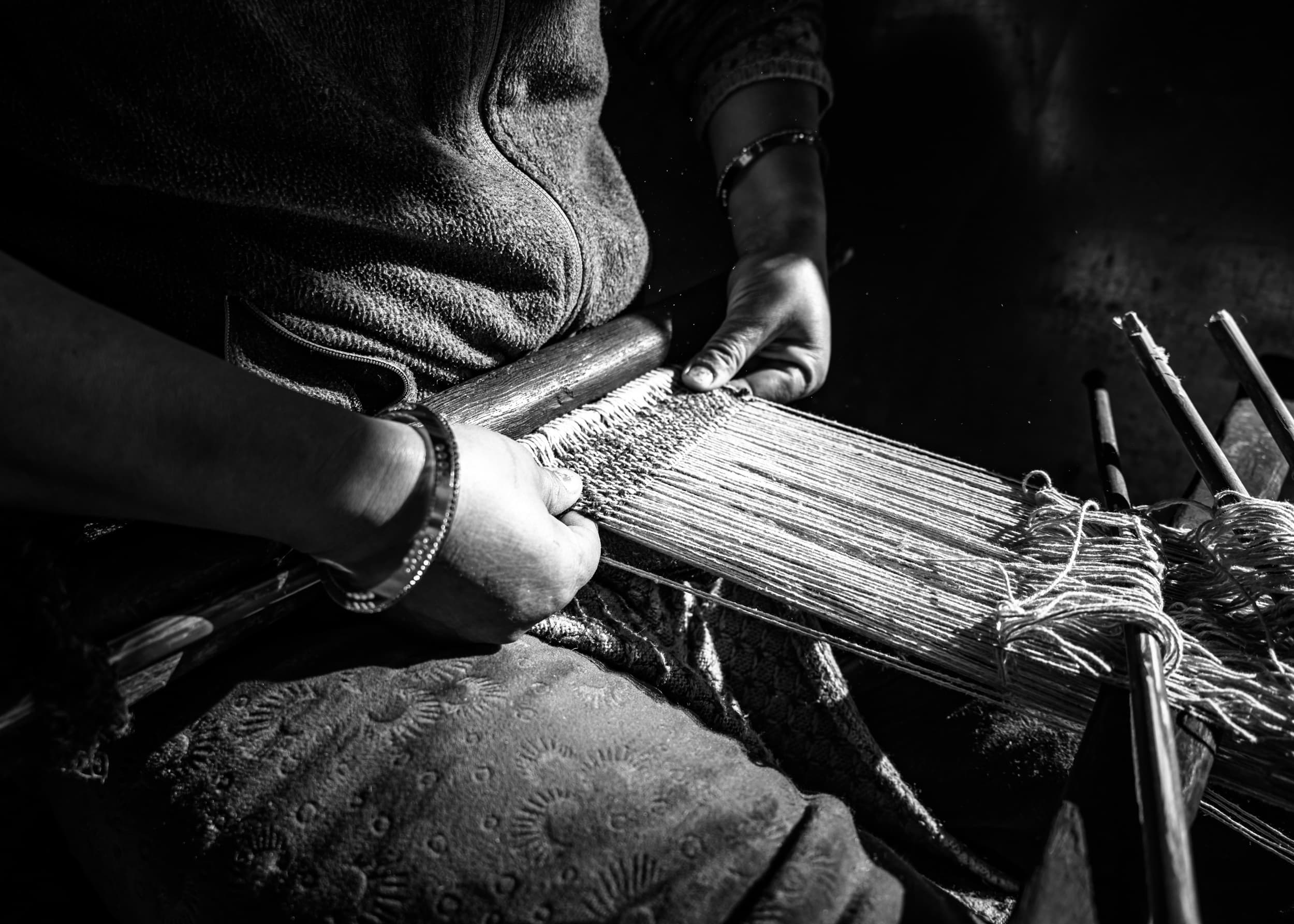 Close-up of two hands working wooden pegs and yarn on a floor loom