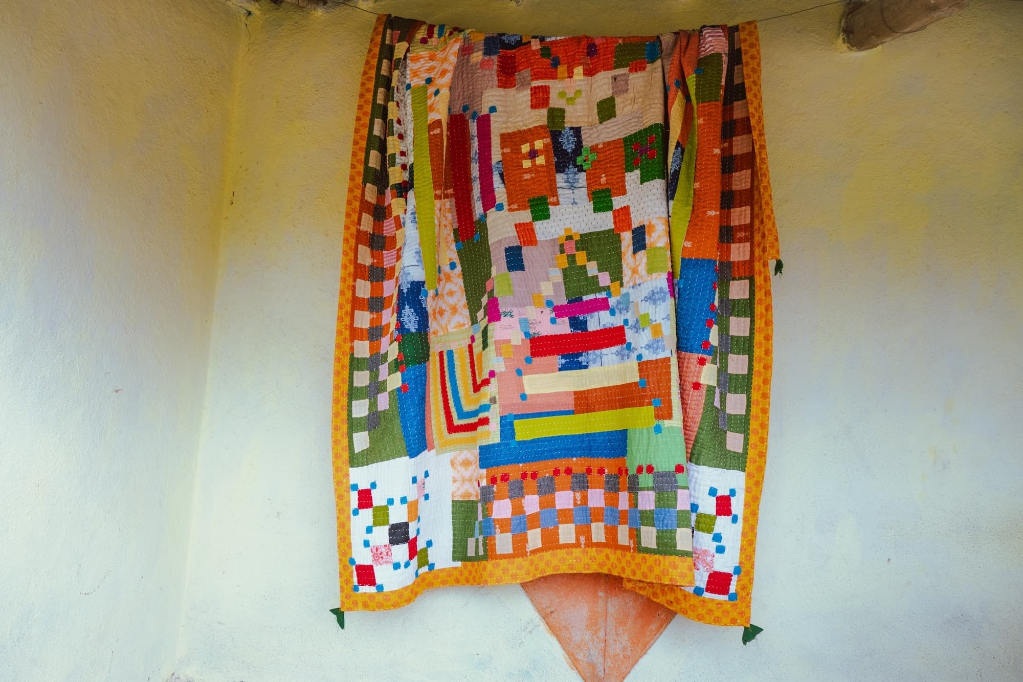 A finished patchwork quilt hanging against a sunlit ochre wall