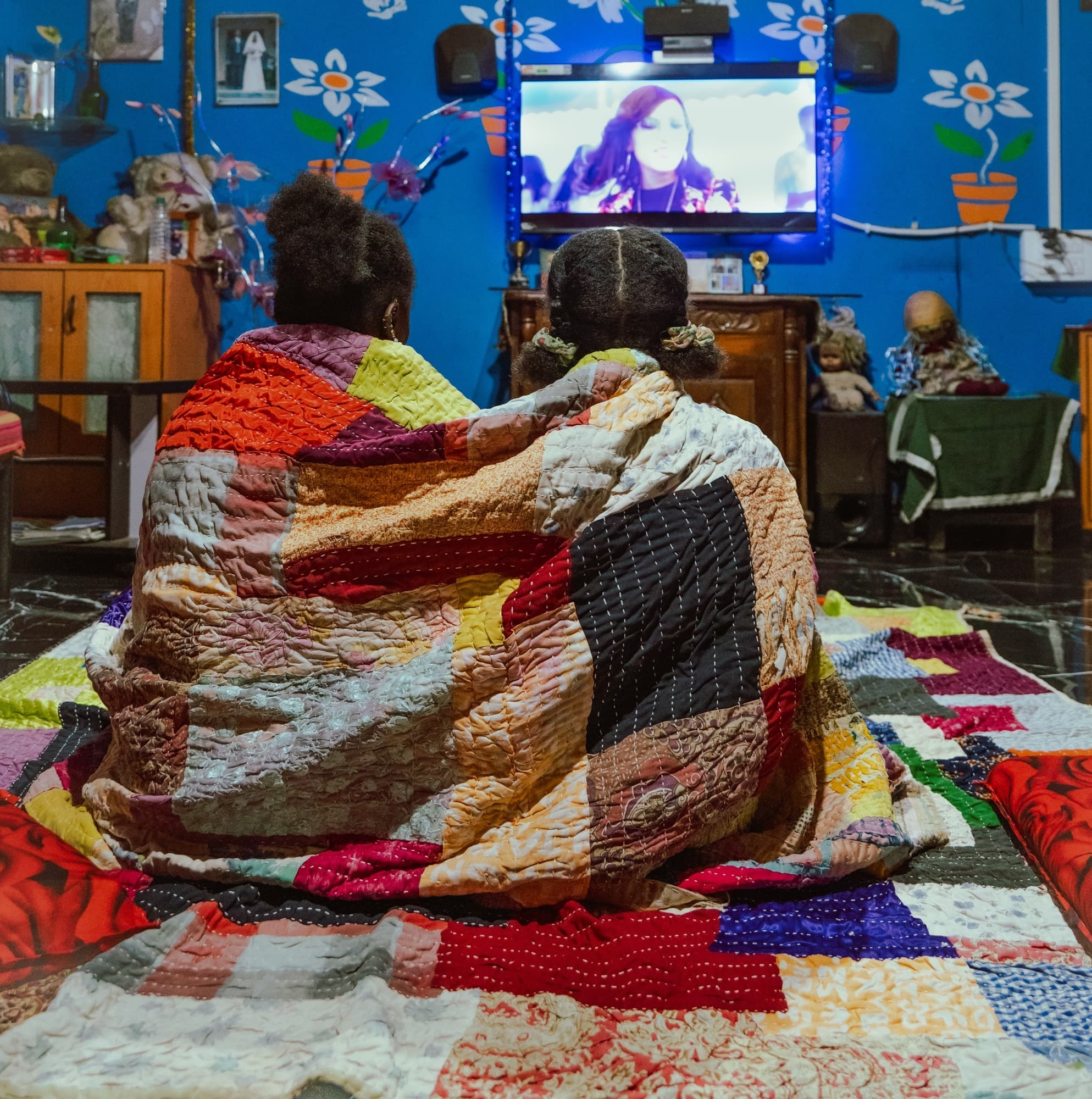 Two children wrapped in a patchwork quilt watching television in a painted room