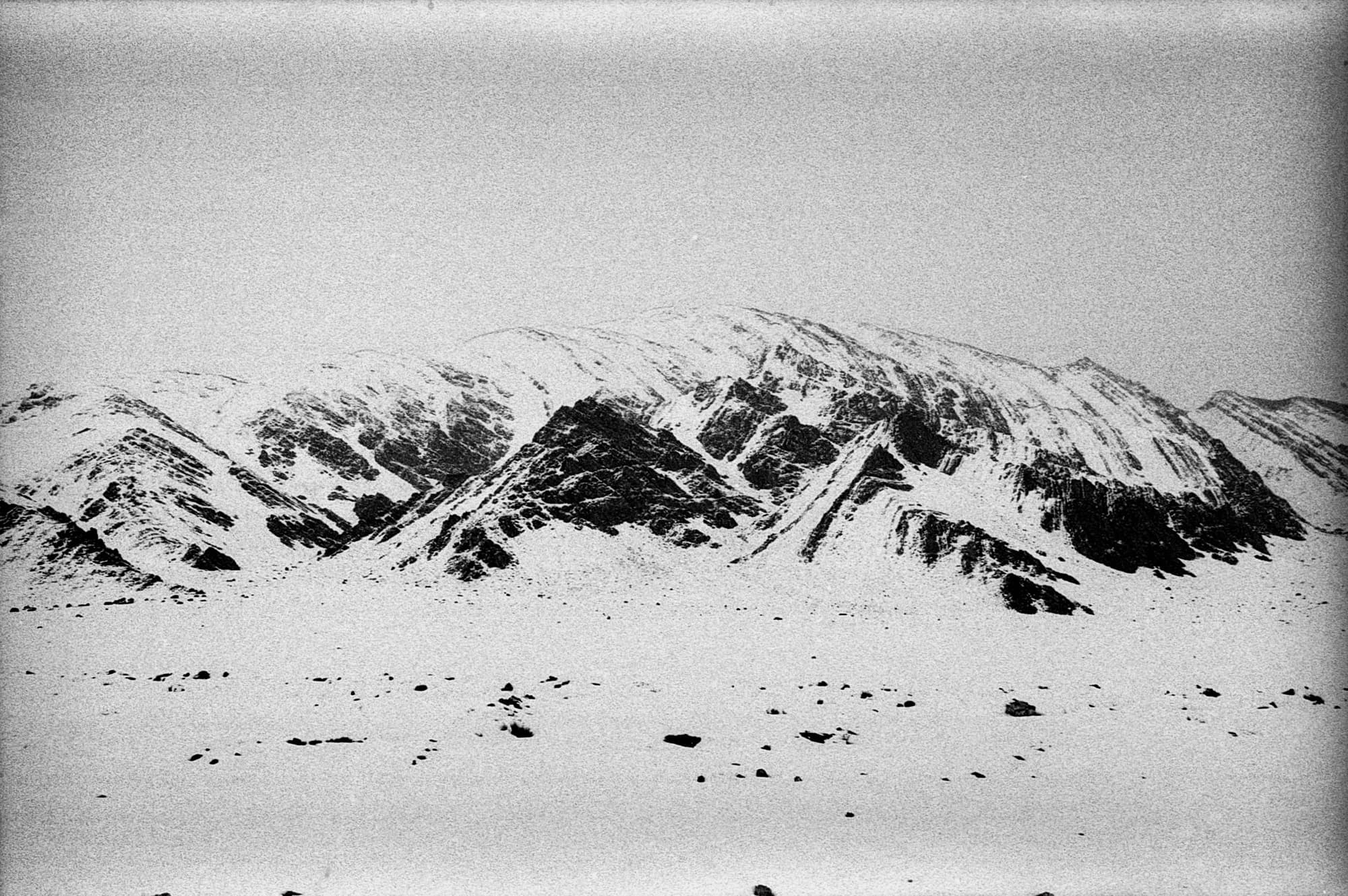 A grainy view of a snow-streaked mountain ridge under an overcast sky