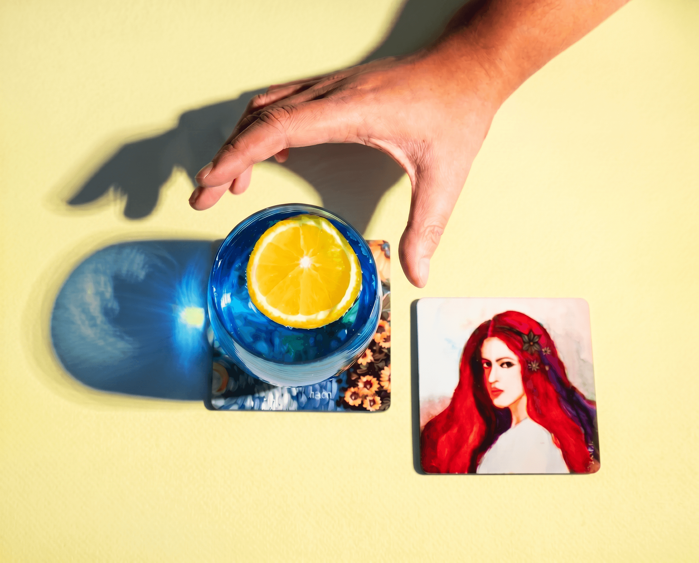 A hand reaching for a blue glass on an illustrated coaster against a lemon-yellow background