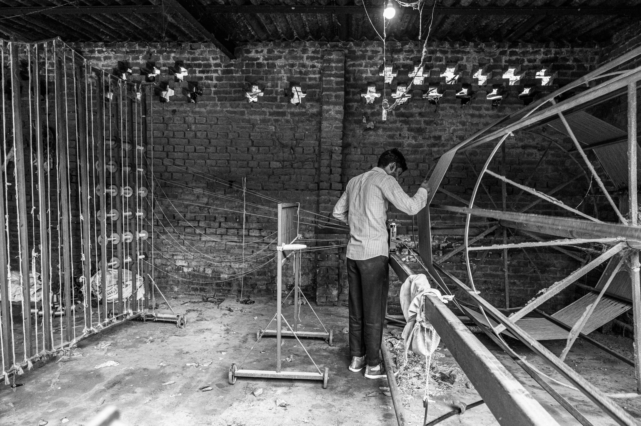 A worker winding yarn onto a large warping wheel in a brick carpet workshop
