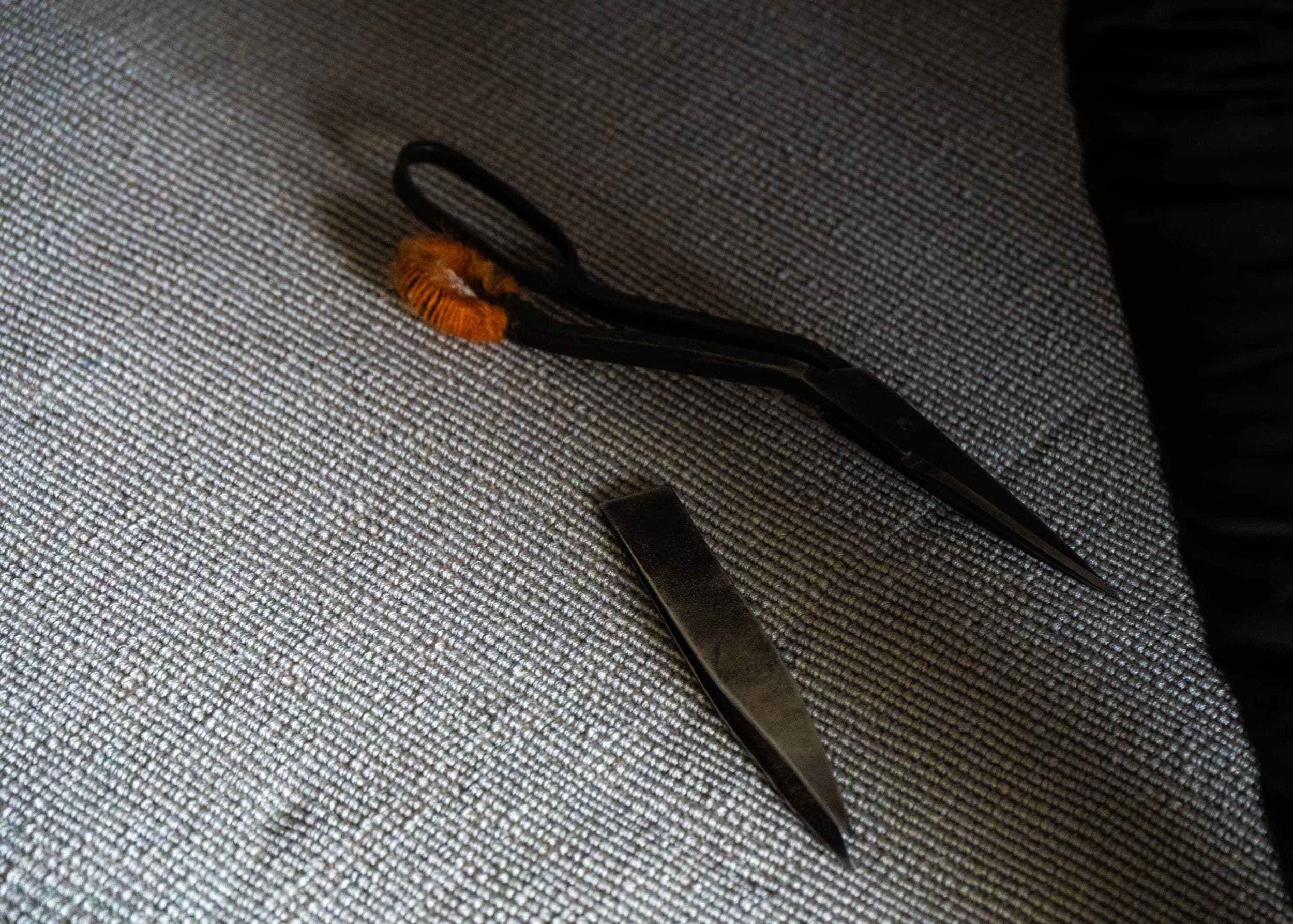 A pair of carpet-trimming scissors resting on a woven carpet surface