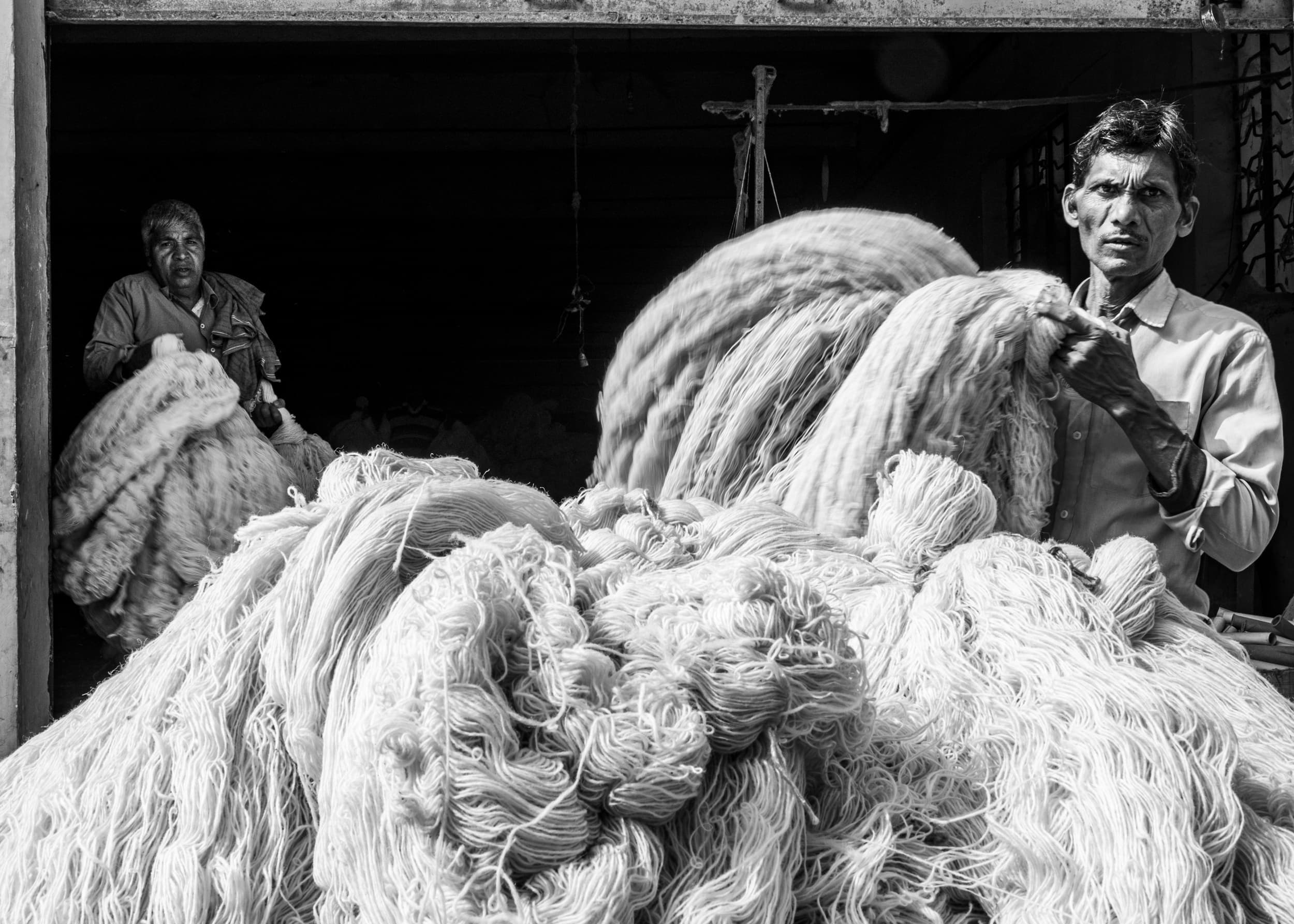 Two men carrying large hanks of raw wool into a carpet workshop doorway